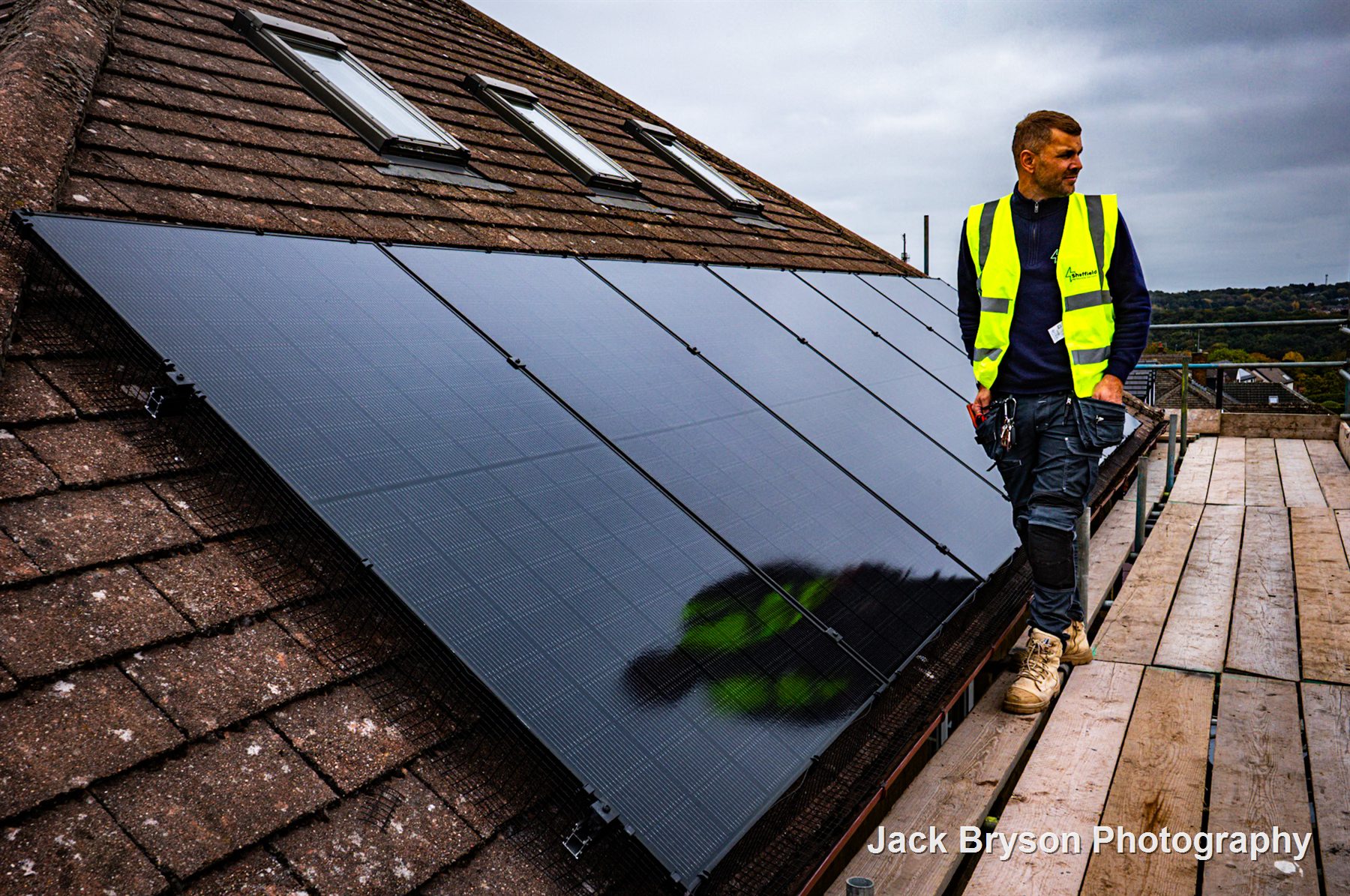 Tradesperson standing beside solar panels on a roof