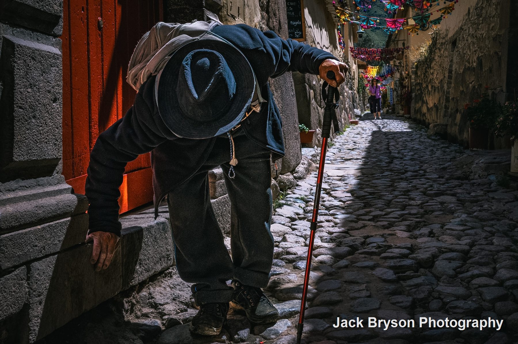 Colour street photograph of a person walking through a narrow cobbled lane