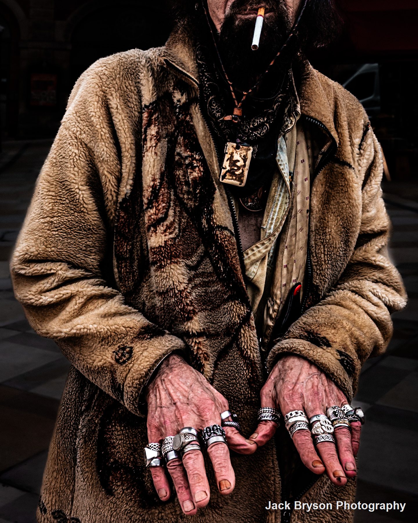 Colour street portrait detail of hands covered in silver rings with a cigarette